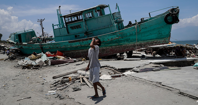 An Indonesian boy drinks water next to a boat that was beached during a tsunami in Palu, central Sulawesi, Indonesia, 02 October 2018